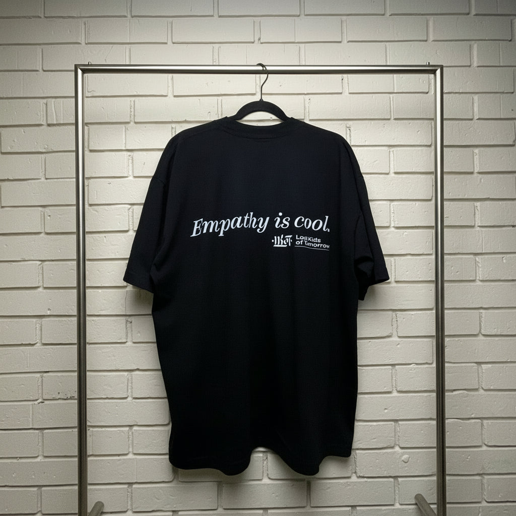 Black t-shirt with 'Empathy is cool' text on a hanger against a white brick wall.